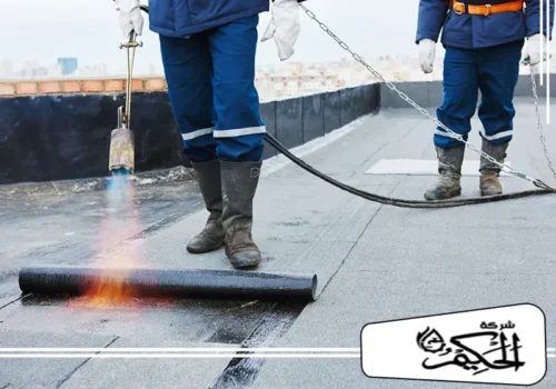 عزل أسطح المنازل والفيلات بالفجيرة تُظهر الصورة عمال بناء يقومون بتركيب لفائف عازلة للأسطح باستخدام شعلة حرارية. يقوم أحد العمال بتسخين اللفافة البيتومينية