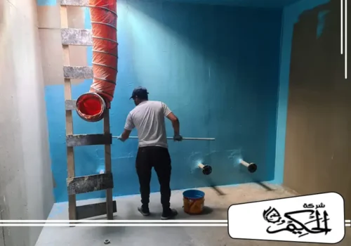 مادة عزل خزانات المياه الارضيه في الفجيرة صورة تُظهر عاملاً محترفاً وهو يطبق طبقة عزل مائي سميكة باللون الأزرق على الجدران الداخلية لخزان أرضي أو حوض تخزين كبير